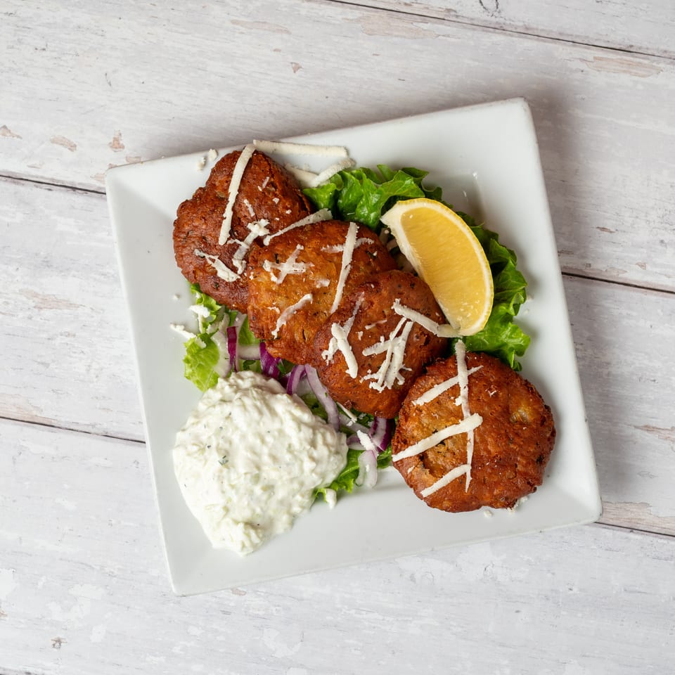Four golden fried patties topped with shredded cheese, served on lettuce with creamy dip and a lemon wedge.