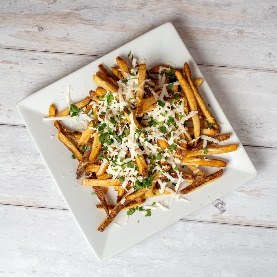 Crispy French fries topped with shredded cheese and chopped parsley on a white square plate.
