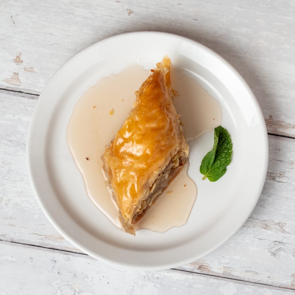 Triangular piece of syrup-soaked baklava garnished with fresh mint on a white plate.
